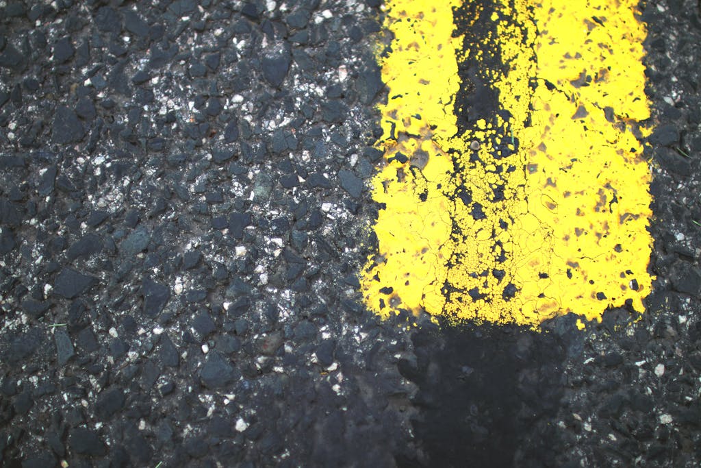 Detailed view of a weathered yellow road marking on rough asphalt surface.